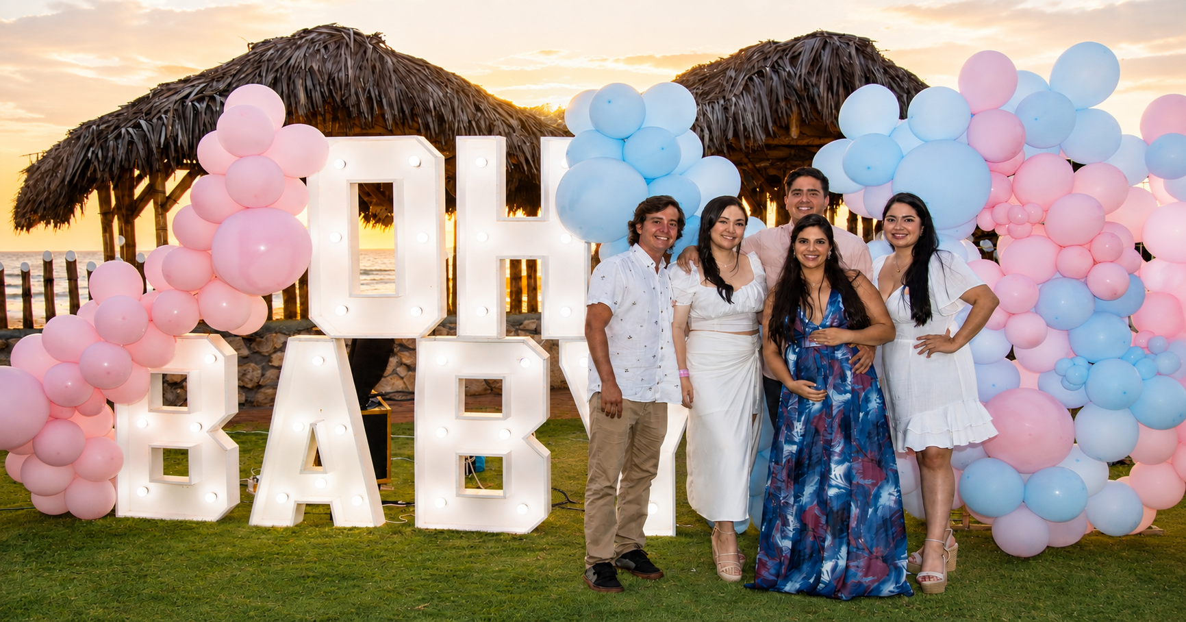 Familia y amigos junto a letras iluminadas OH BABY y globos rosados y celestes durante una revelación de sexo en Playas, Ecuador.