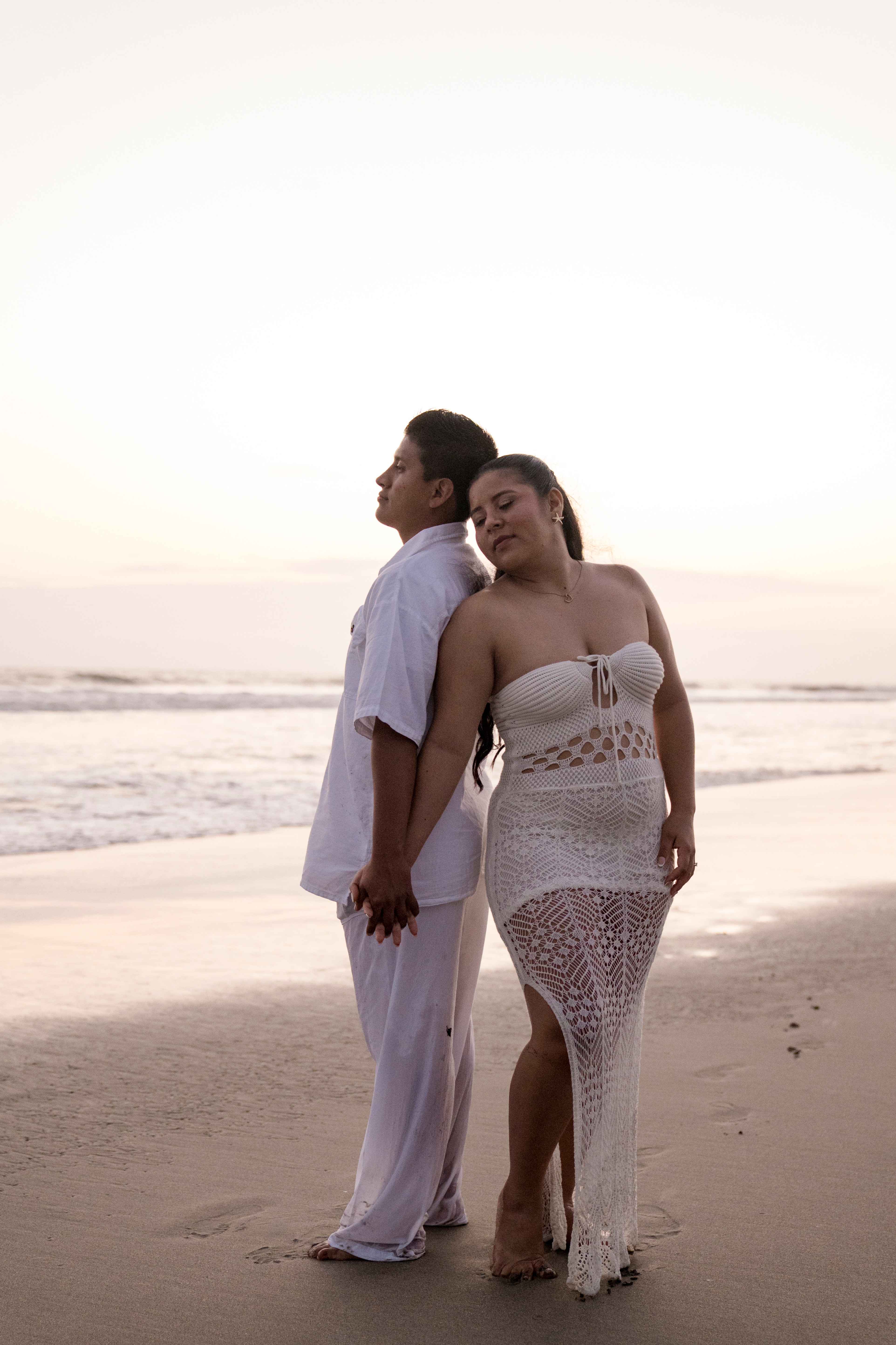 Jarny y Adriana caminando abrazados por la playa al atardecer, celebrando su compromiso.
