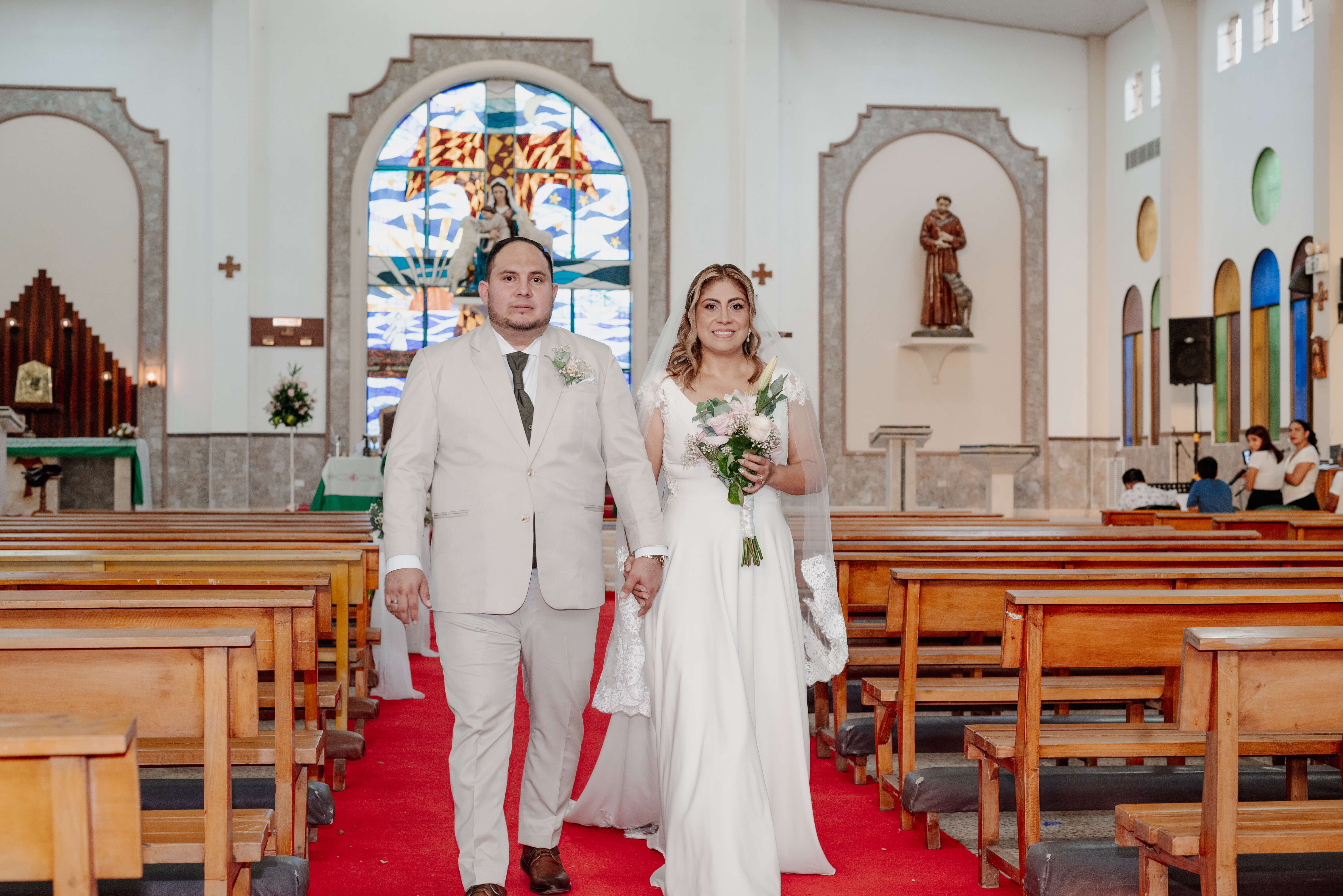 Ingrid y Diego caminan tomados de la mano por el pasillo de la iglesia después de su ceremonia de boda.
