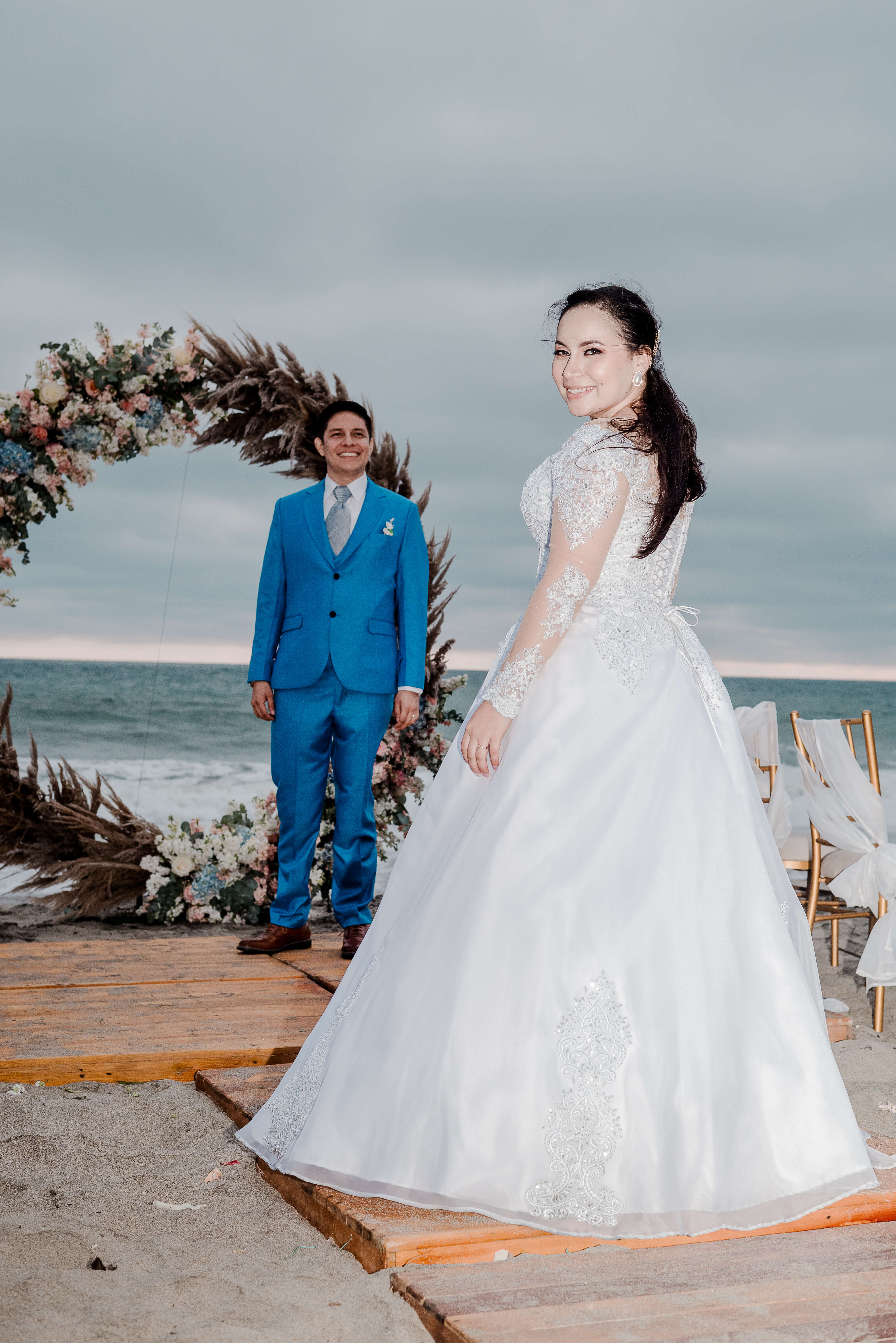 Kattya y Freddy bajo un arco floral durante la ceremonia frente al mar en Karibao.