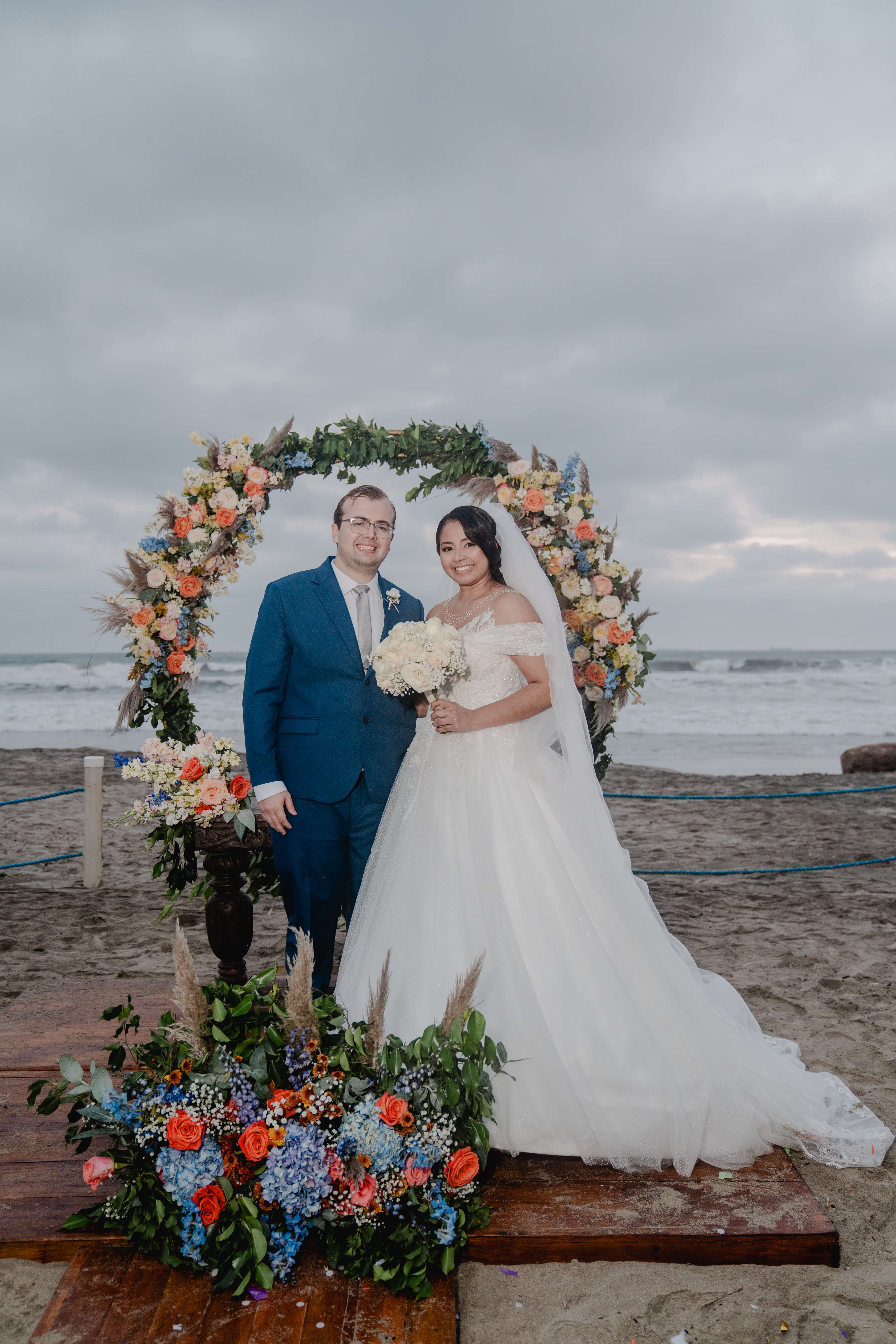 David y Linda en la ceremonia bajo el arco de flores frente al mar en Playas.