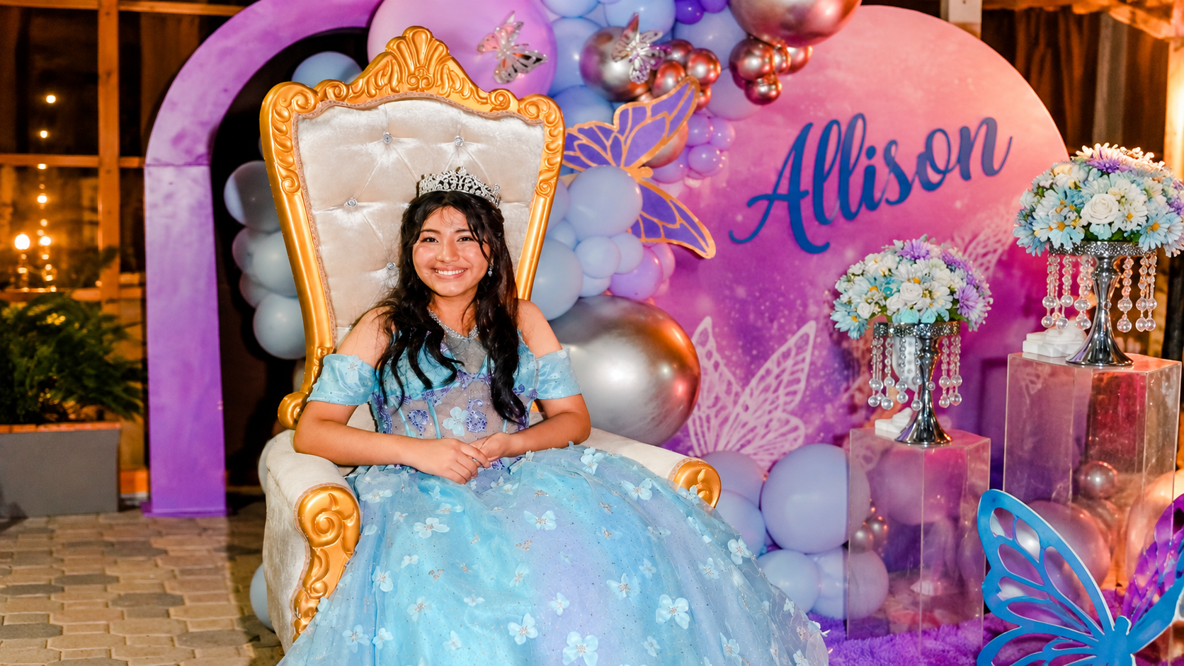Allison luciendo su vestido azul de quinceañera sentada en un trono decorado durante la celebración de sus XV.