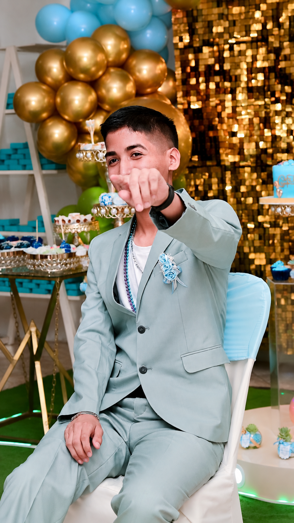 Josué sentado frente a la decoración de sus XV, señalando hacia la cámara durante la celebración.