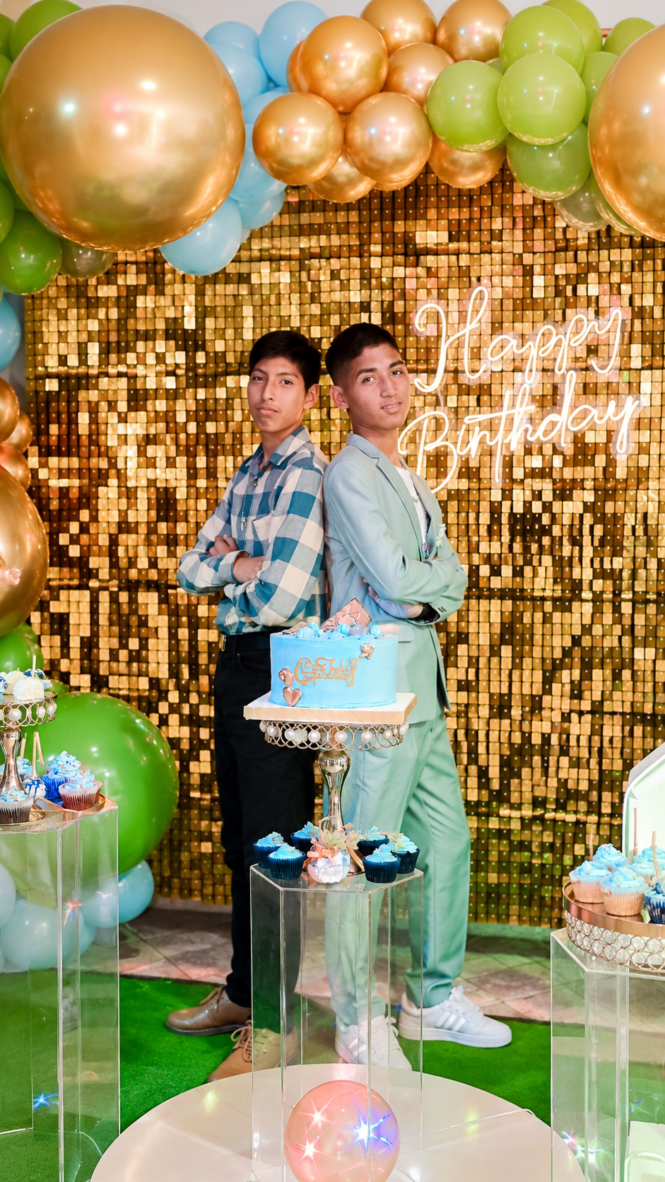 Josué y su hermano posando juntos frente a la decoración dorada de la celebración.