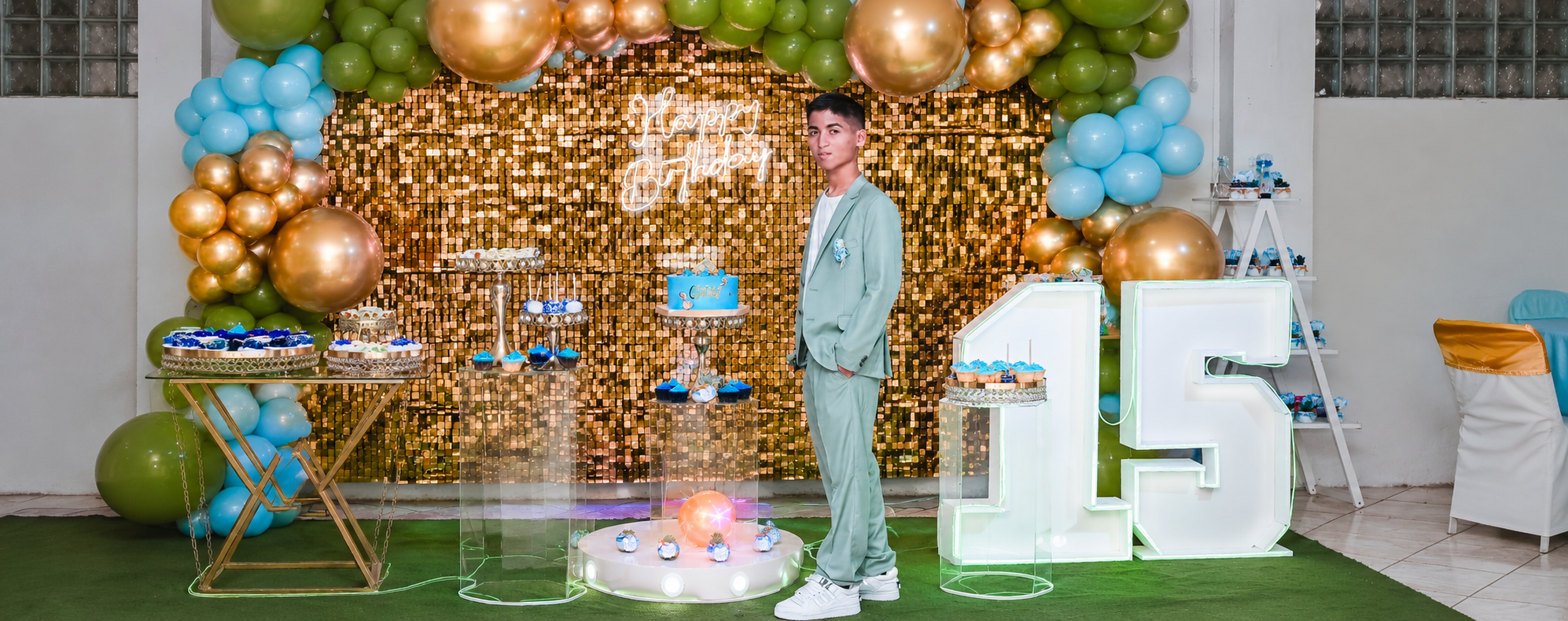 Josué celebrando sus XV con traje verde claro frente a una decoración de globos y fondo dorado.