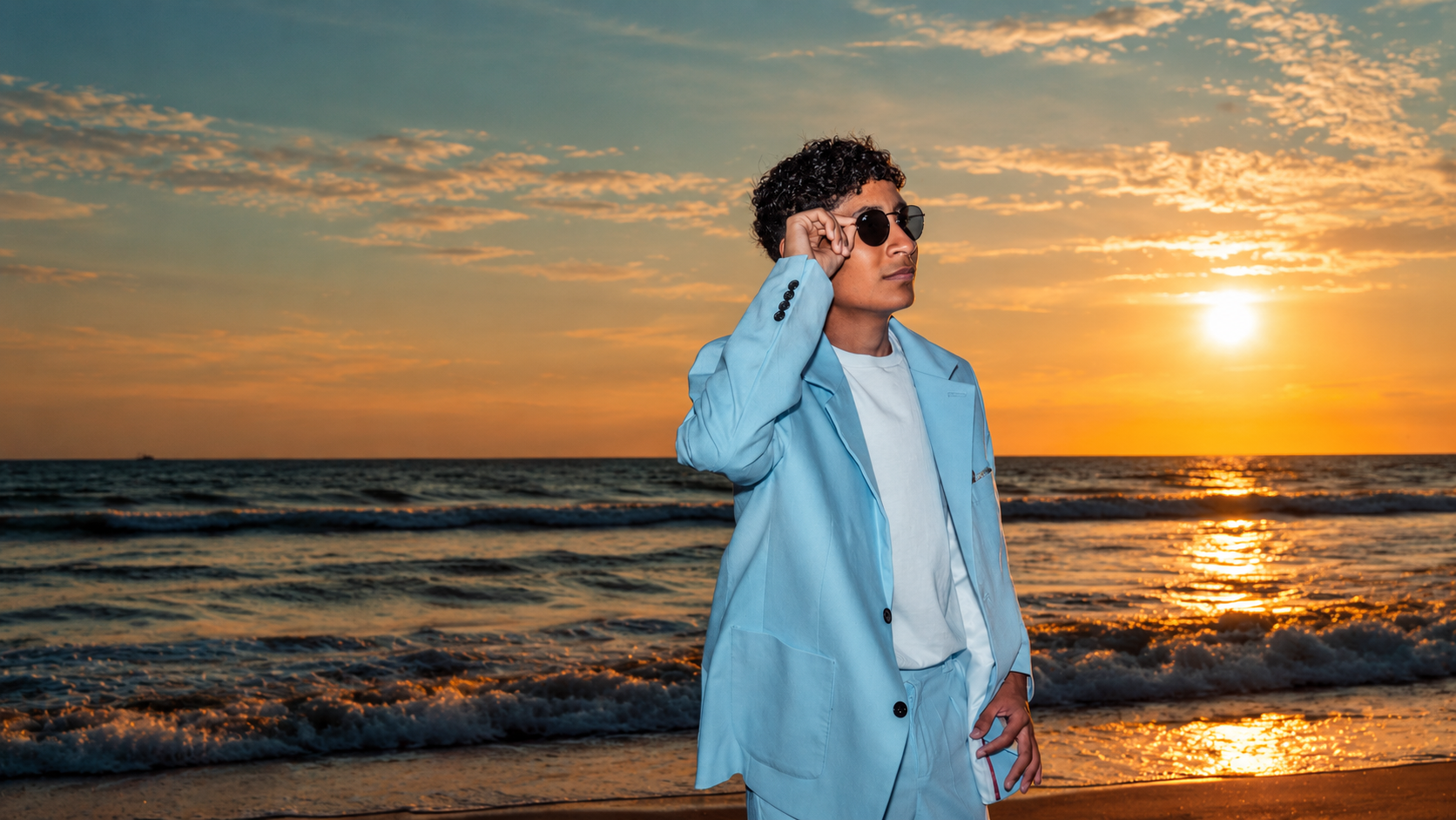 Joven con traje azul claro y gafas de sol frente al mar durante una sesión de fotos de XV años al atardecer en Playas, Ecuador.