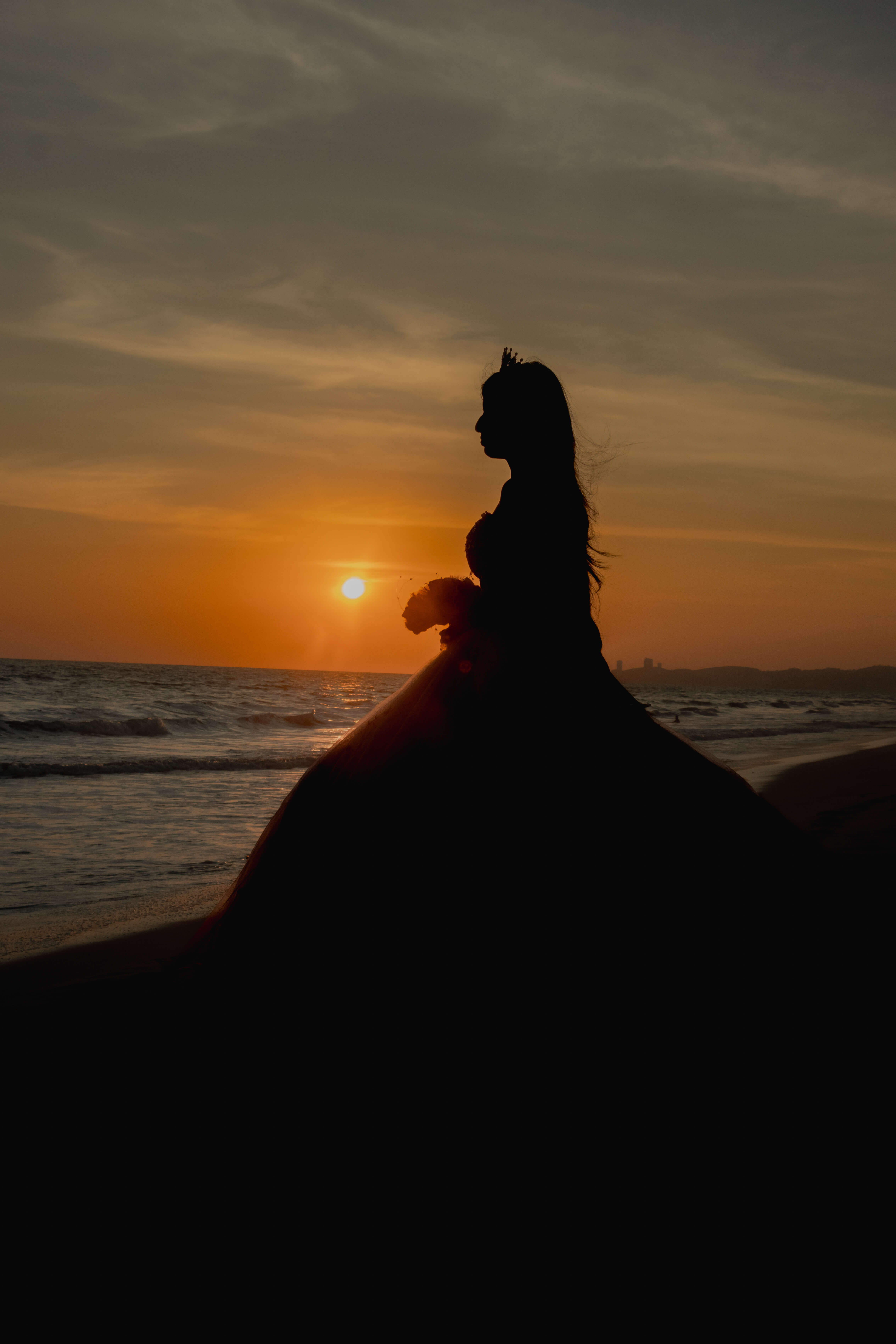 Silueta de una quinceañera con vestido pomposo en la playa durante un atardecer dorado en el mar.