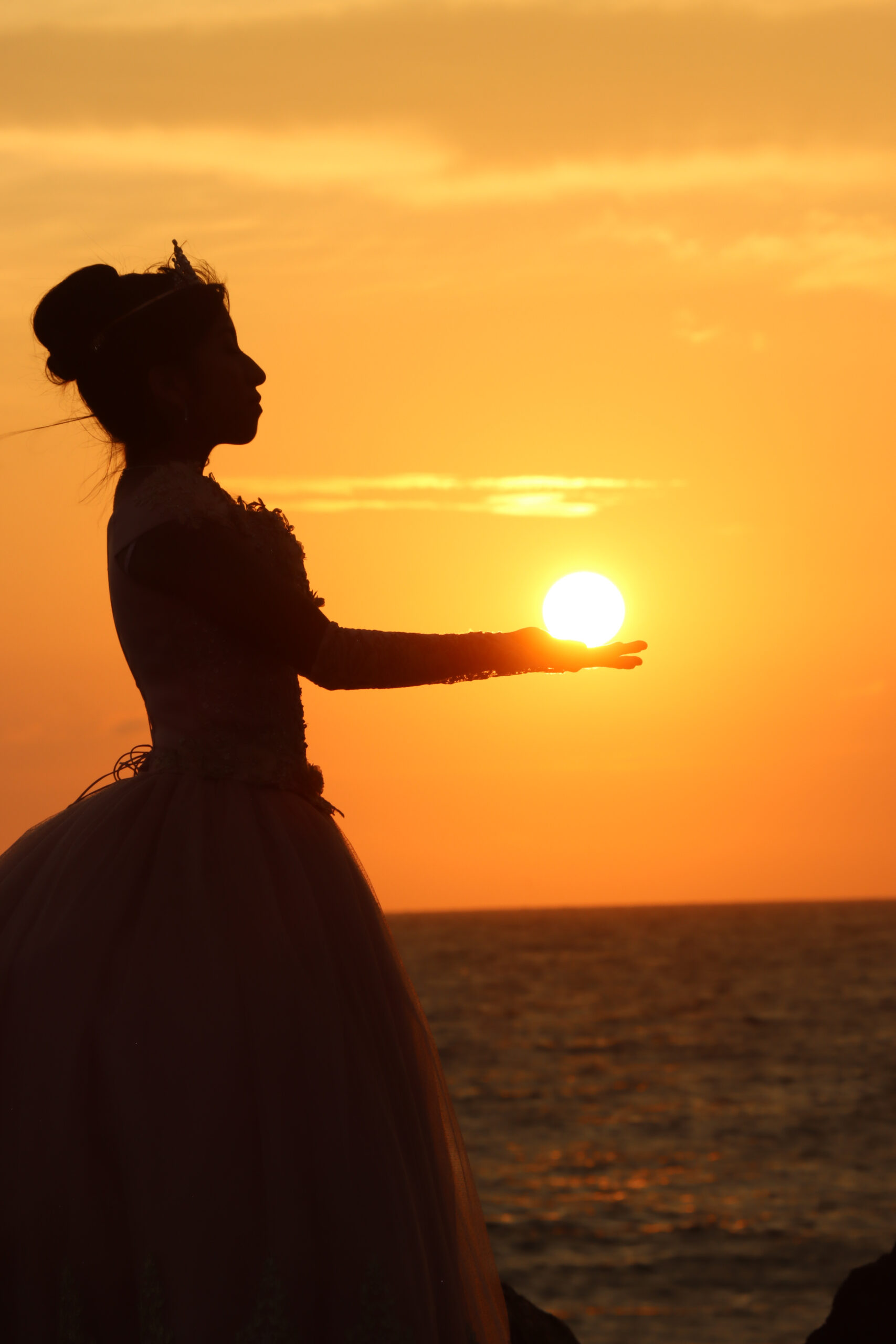 Sesión de fotos de quinceañera sosteniendo el sol en sus manos durante el atardecer en Ocean Club, Playas Ecuador. Capturado por Ola Digital Playas.